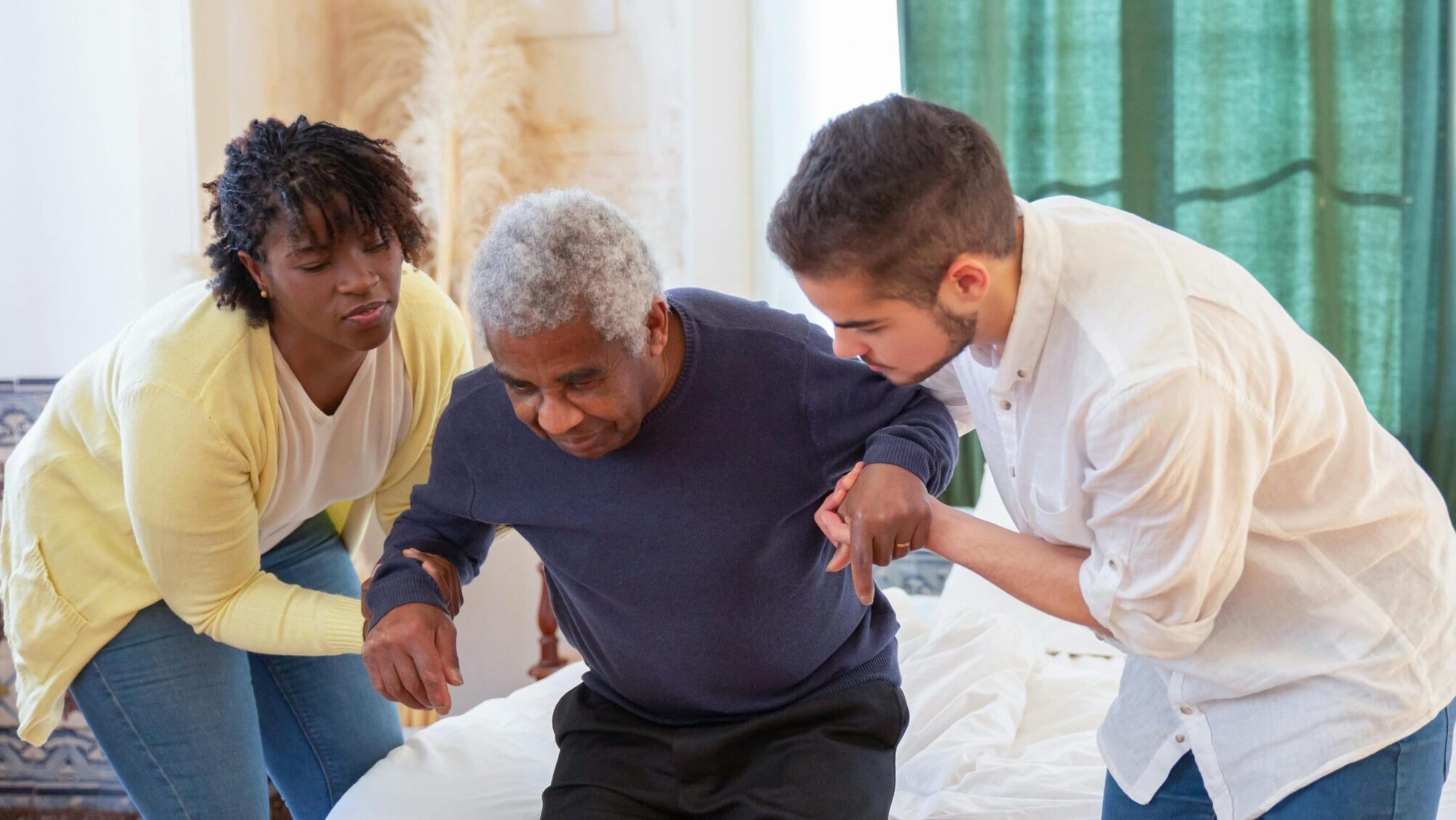 An elderly man receiving assistance from caregivers in a cozy home environment.